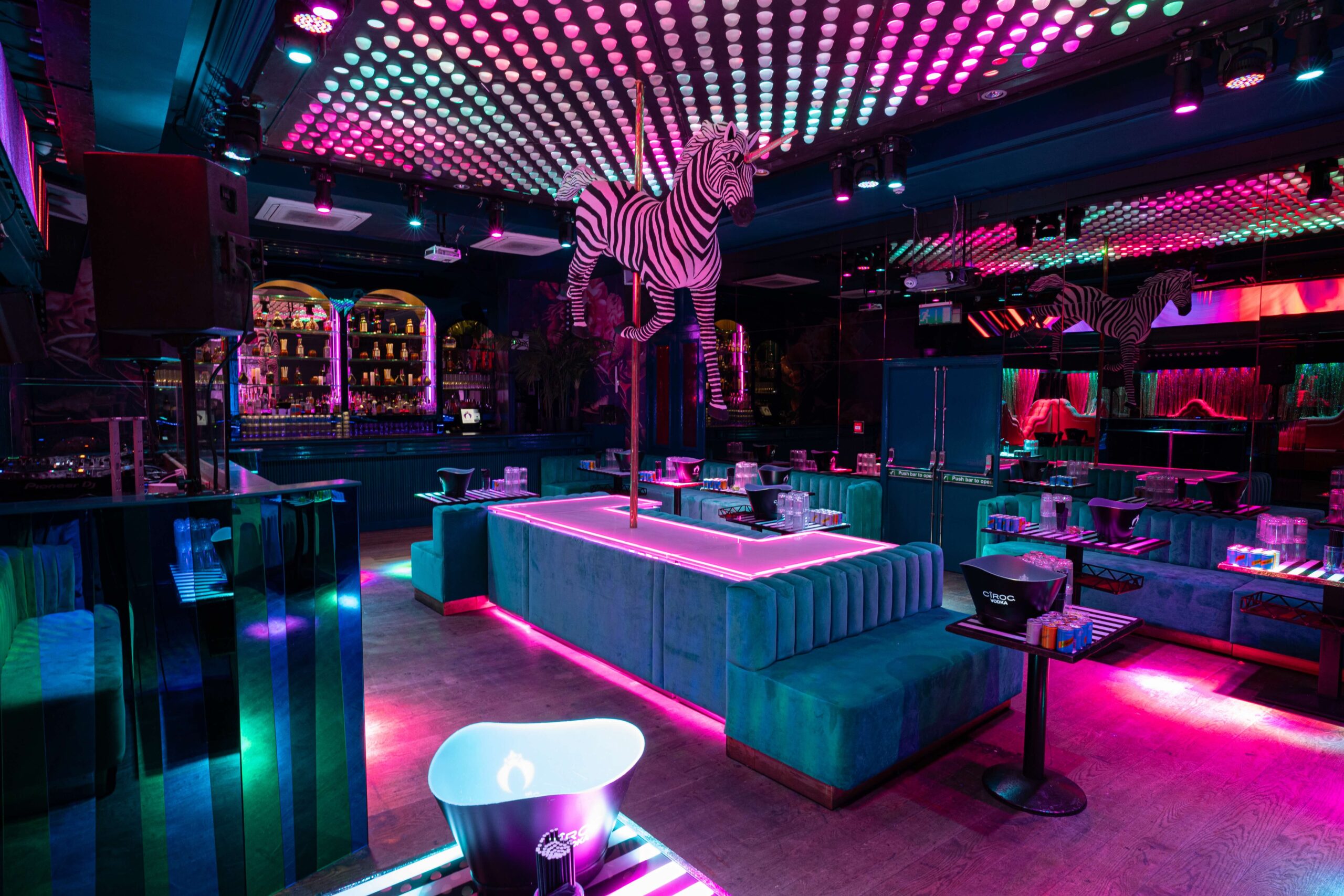 Neon-lit bar with turquoise booths, central stage with zebra statue and colourful lighting