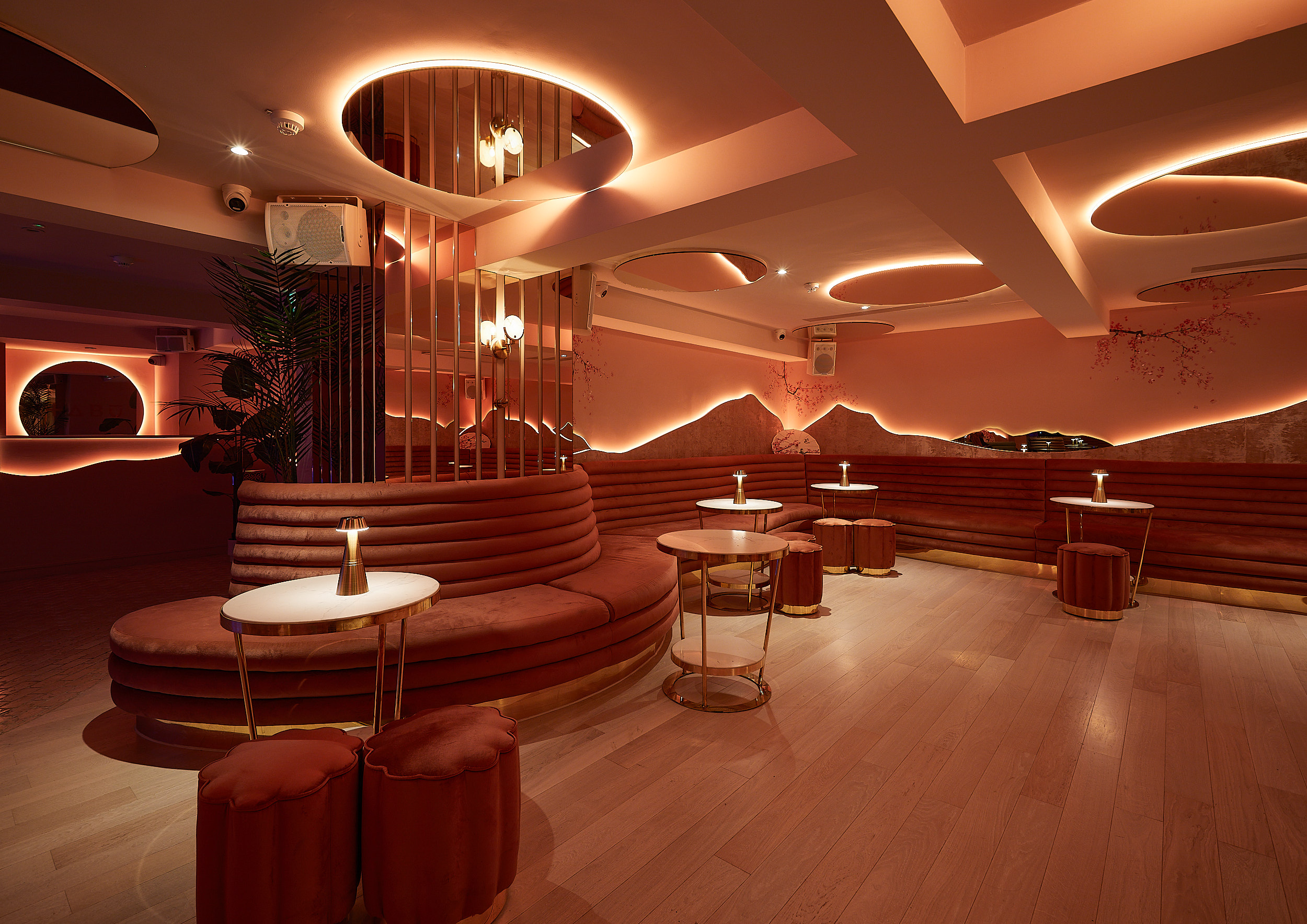 Modern lounge at Yuki featuring circular banquette seating, ring ceiling lights, red velvet stools and warm wood accents