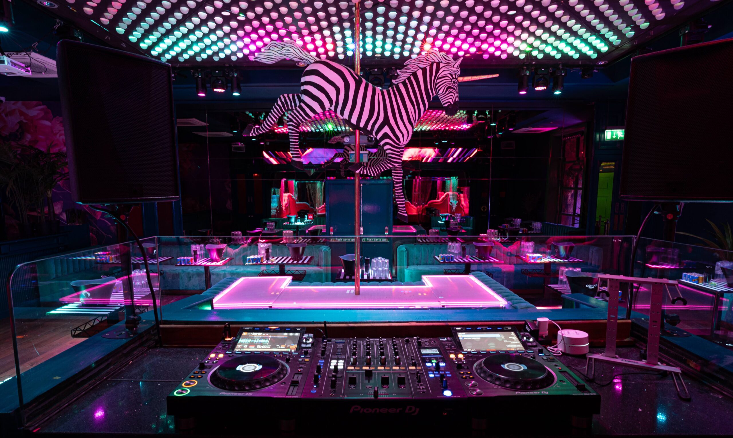 Zebra statue above circular pole stage with neon lighting behind DJ booth at nightclub