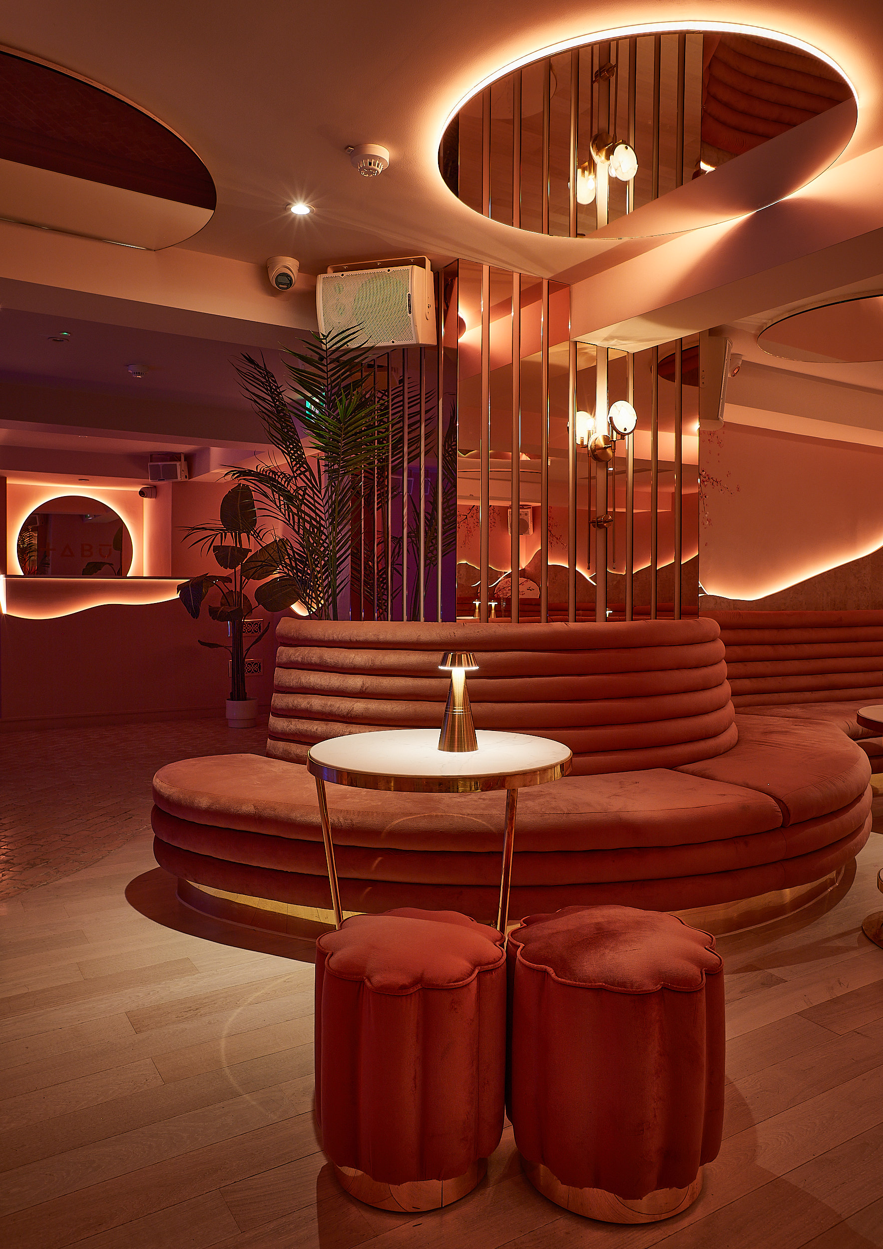 Warmly lit bar at Yuki with circular banquette seating, red velvet stools, palm plant and mirrored columns