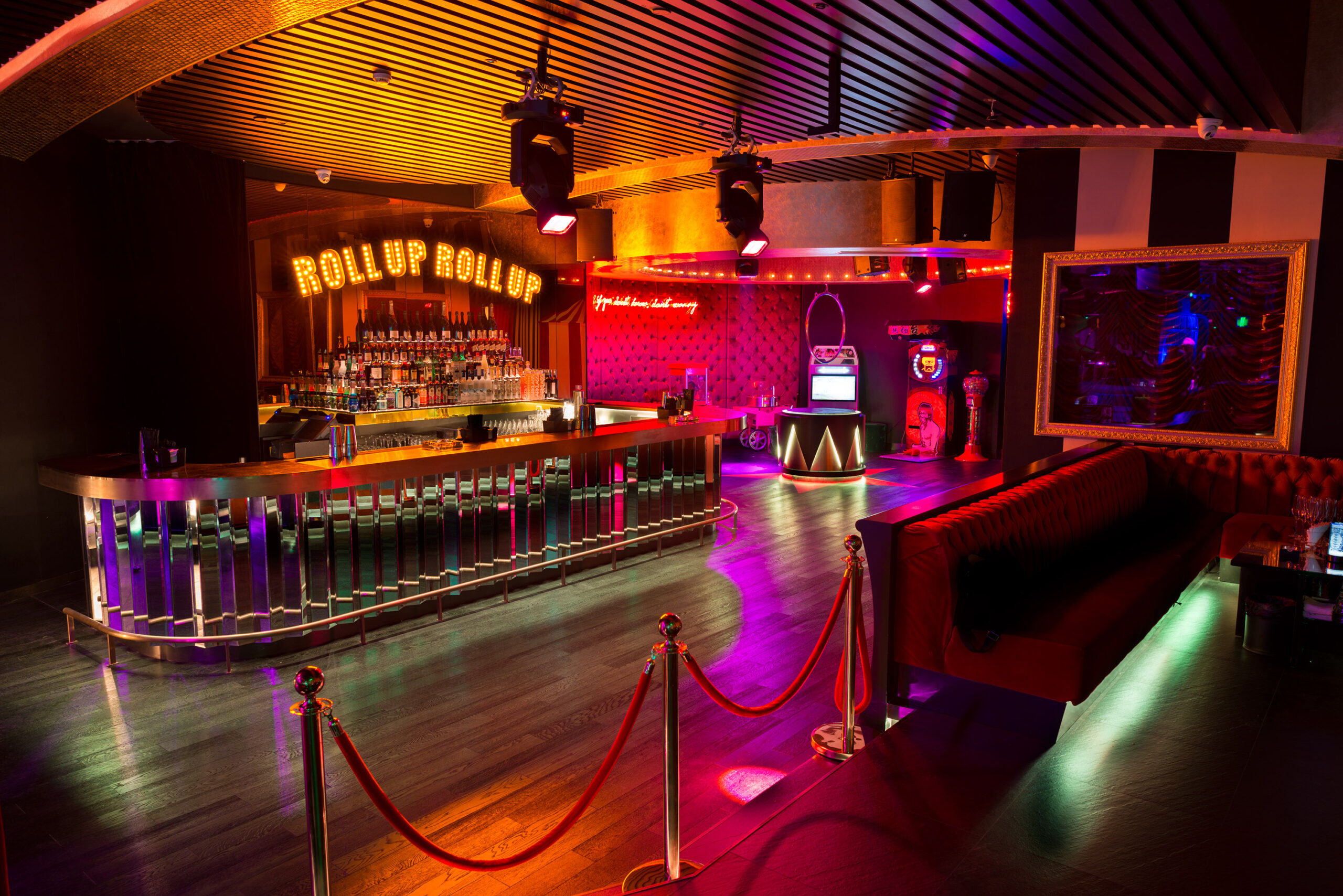 Retro circus-themed bar with curved reflective counter, 'Roll Up Roll Up' sign and jukebox