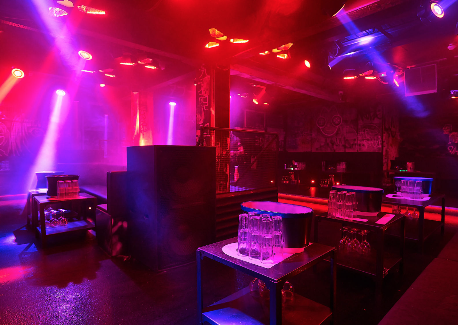 Nightclub interior at Tabu with neon pink and blue lighting, DJ booth, high tables and bar stools