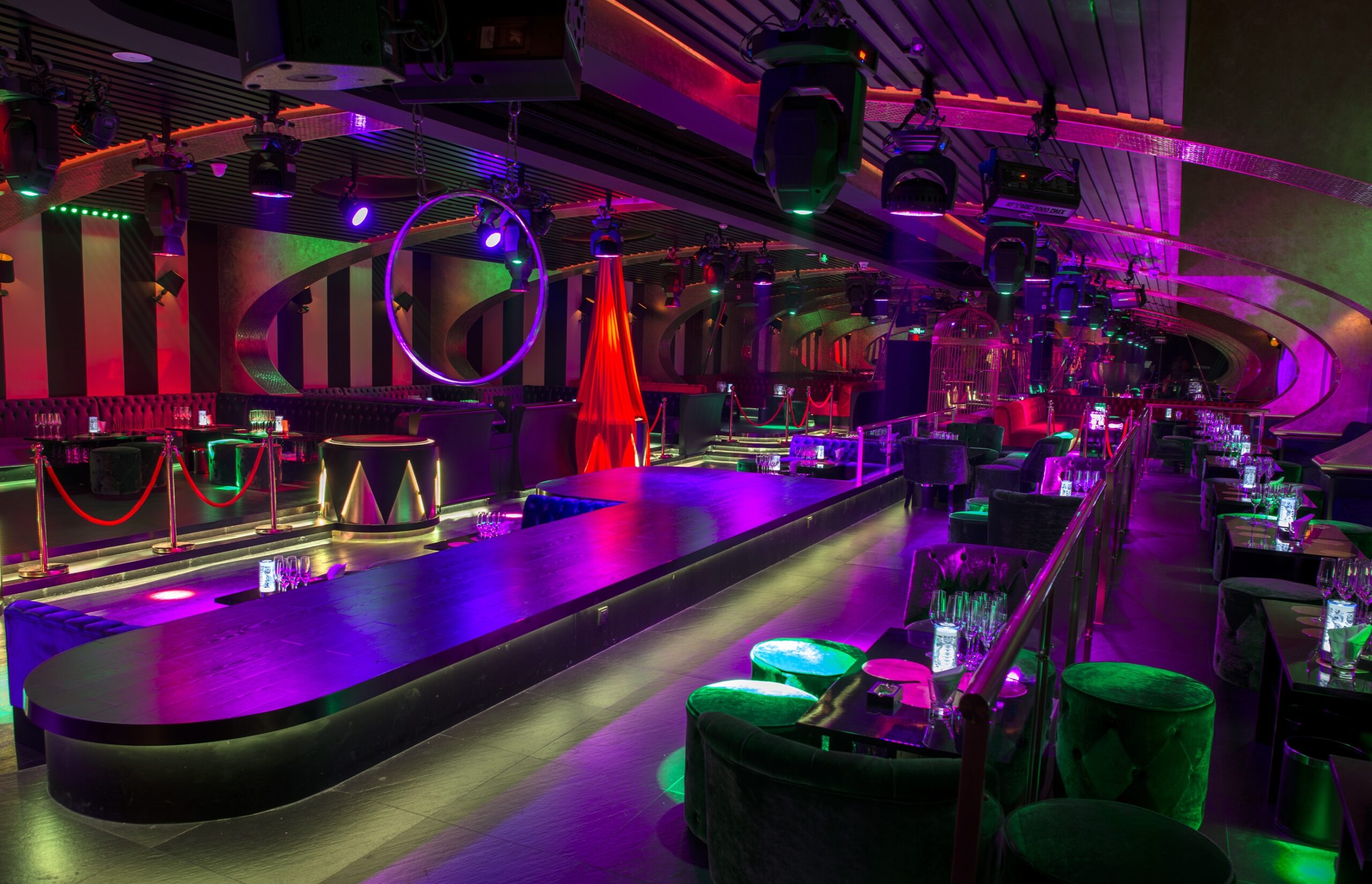 Long runway stage in nightclub with neon purple and green lighting and circular hanging hoops