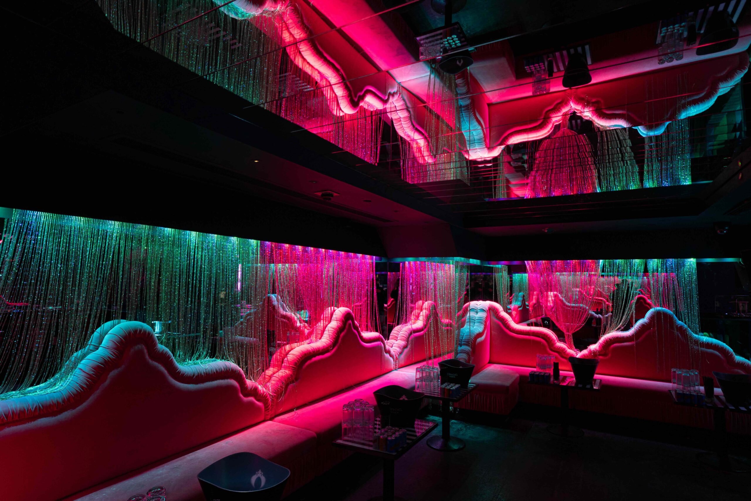 Modern bar interior with undulating pink and turquoise LED wave lighting along walls and seating booths