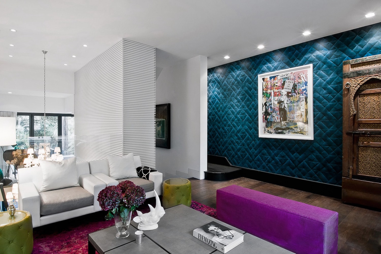 Modern living room with white sofas, purple bench, teal quilted feature wall and carved wooden door