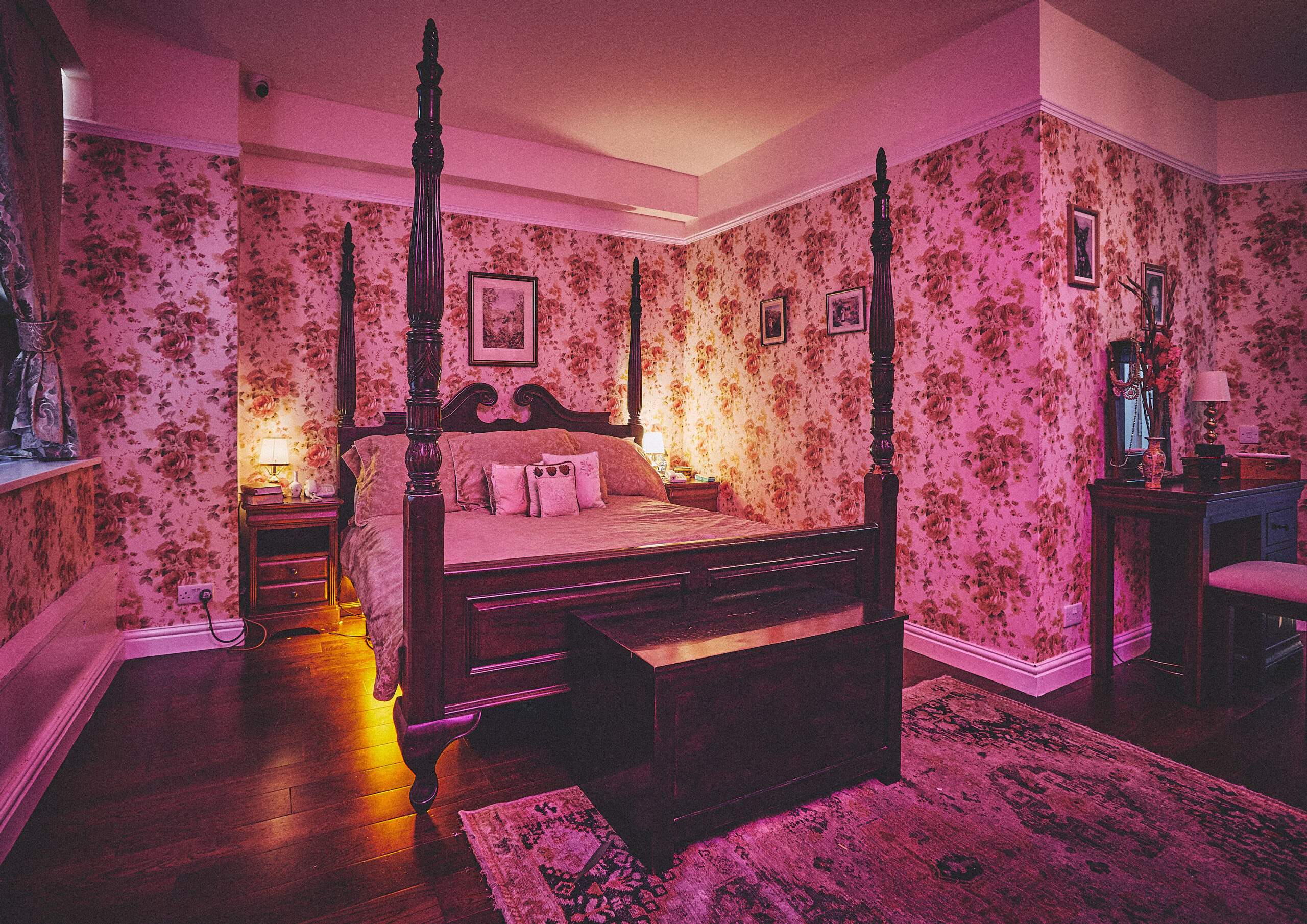 Vintage bedroom at House Party Soho with four-poster bed, pink floral wallpaper and moody lighting